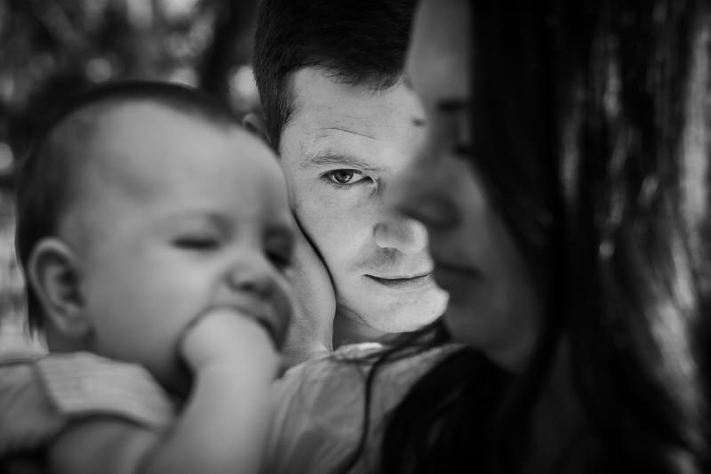 mother holding baby in the foreground and dad in focus in the background looking at them